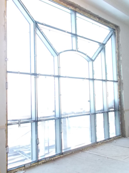 Панорамное крупногабаритное бронированное витражное окно сложной формы с пуленепробиваемыми стеклопакетами в процессе монтажа.